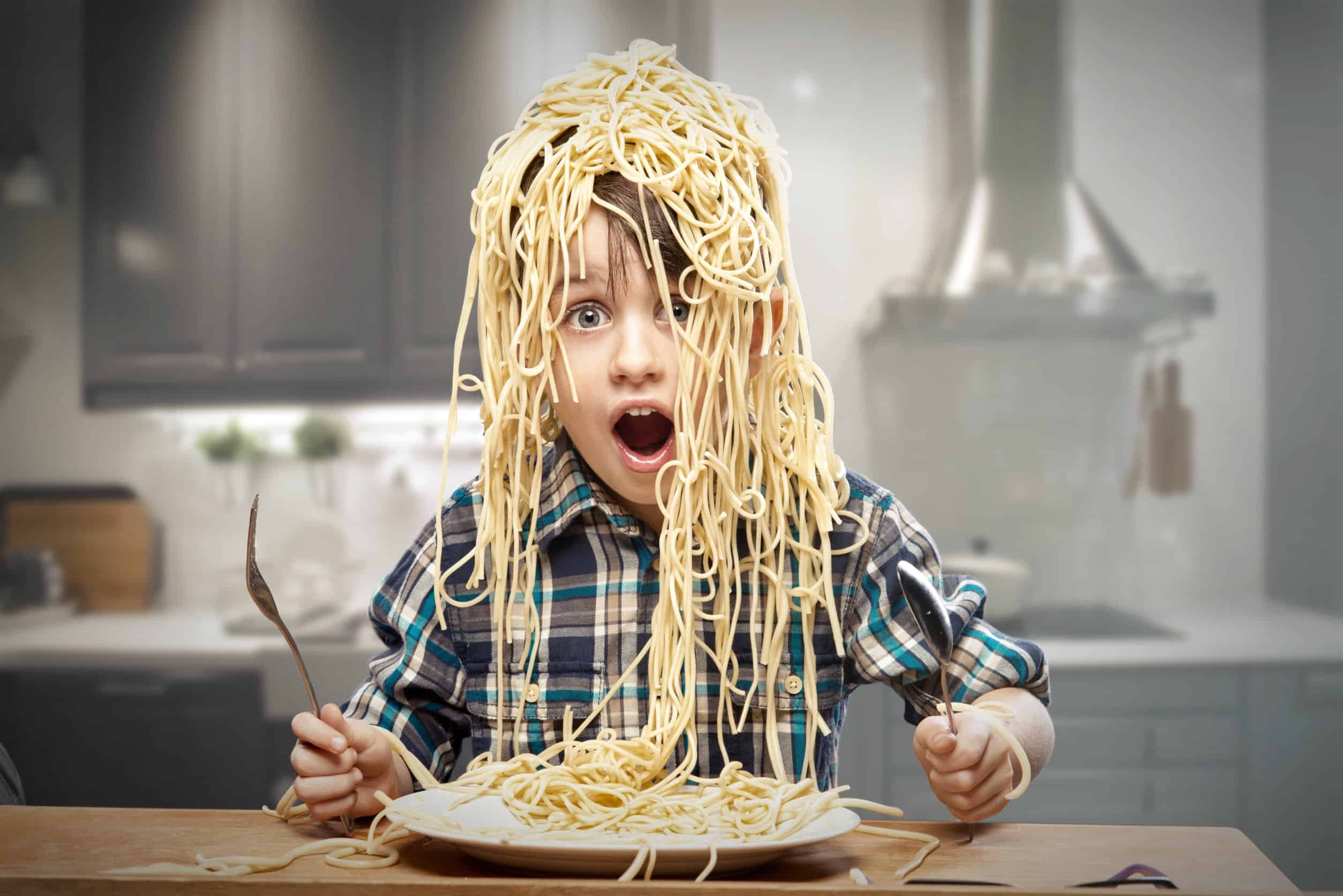 Young boy looking surprised with spaghetti tipped over his head